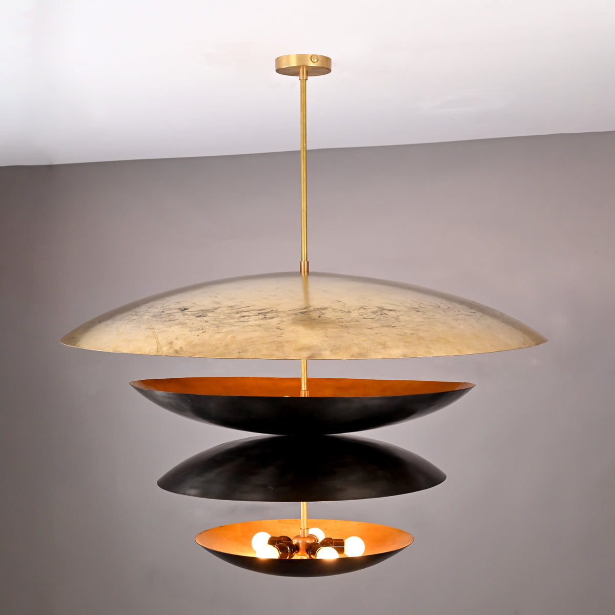 Front angle of illuminated 10-light layered disc chandelier with warm inner glow and contrasting black and gold brass bowls.