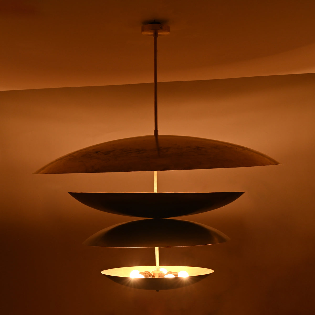 Warm night view of 10-light layered disc brass chandelier with sculptural stacked bowls glowing softly in ambient lighting.