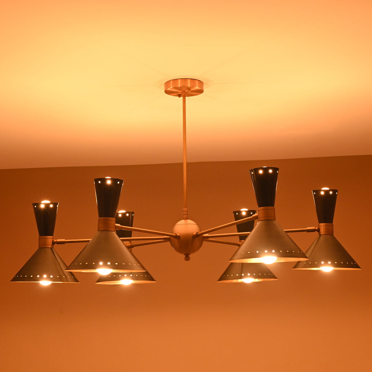 Side angle of illuminated 12-light brass and black cone chandelier with brushed brass arms and warm diffused lighting.