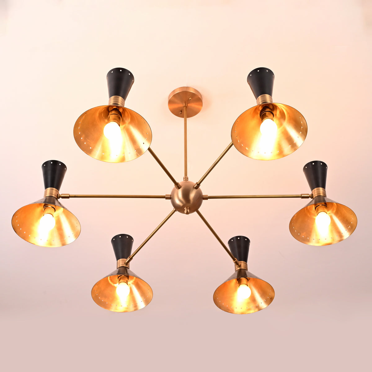 Bottom view of 12-light brass and black mid-century cone chandelier with glowing gold interiors and warm light output.
