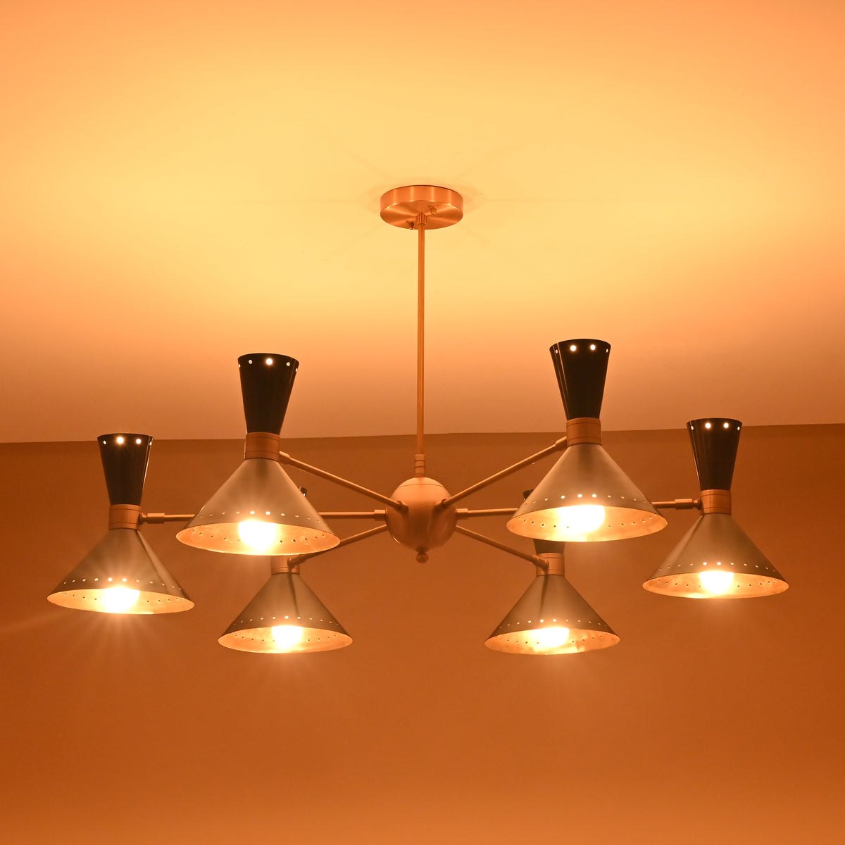 Warm ambient ceiling glow from 12-light brass and black mid-century chandelier with cone-shaped perforated shades.