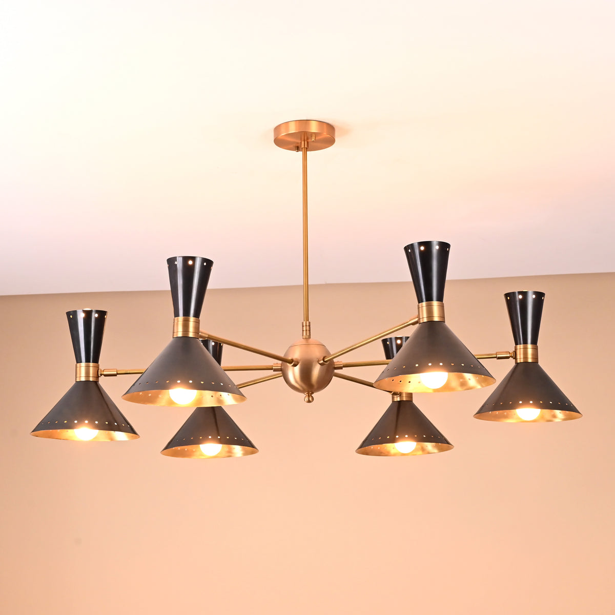 Illuminated 12-light brass and black cone chandelier showcasing warm ambient lighting and perforated mid-century shades.