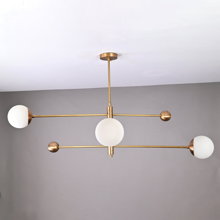 Handmade 3-light brass chandelier featuring balanced linear arms and frosted globes, mid-century modern ceiling fixture.