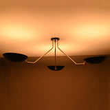 Three-light black and brass chandelier with warm upward glow and sculptural asymmetrical arms.