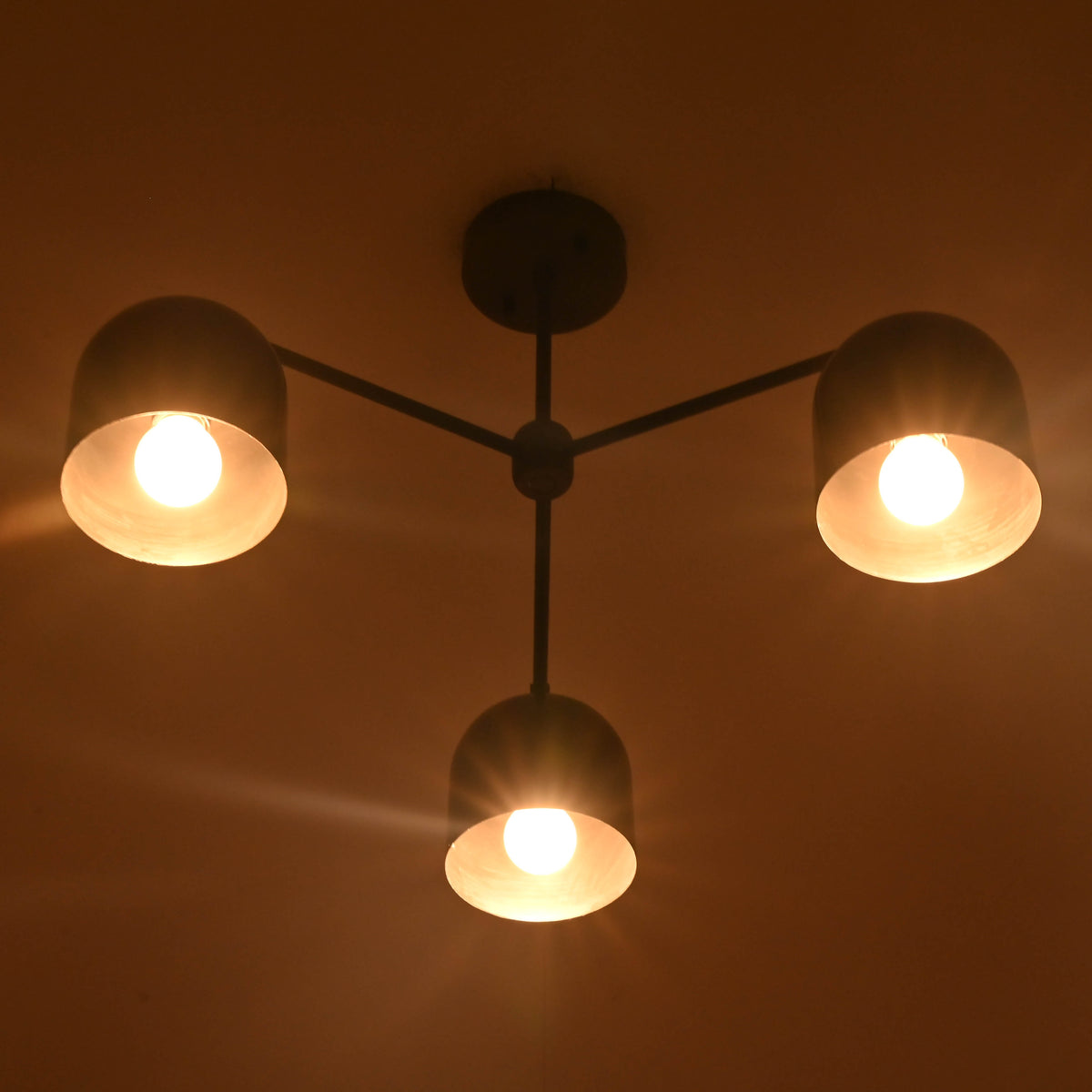 Bottom view of a 3 light brass chandelier highlighting bowl shades and warm downward lighting.