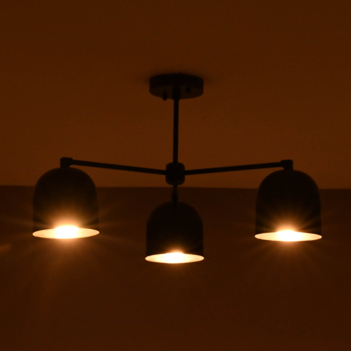 3 light brass bowl chandelier illuminated with warm ambient lighting in a dark interior setting.