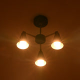 Black and brass 3 light flush mount chandelier glowing warmly in dark room interior