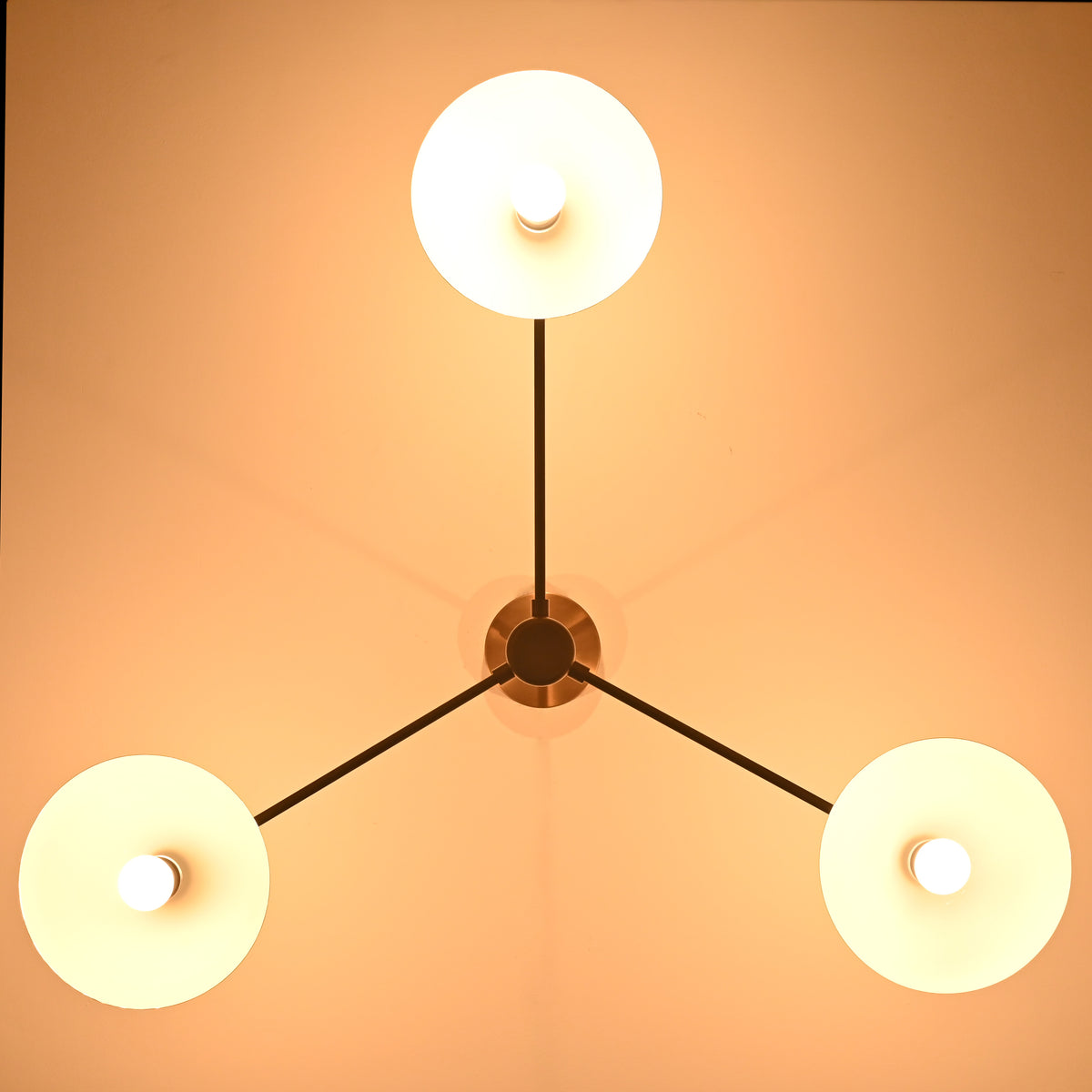 Bottom view of brass 3-light chandelier illuminated with warm lighting and white inner shades.