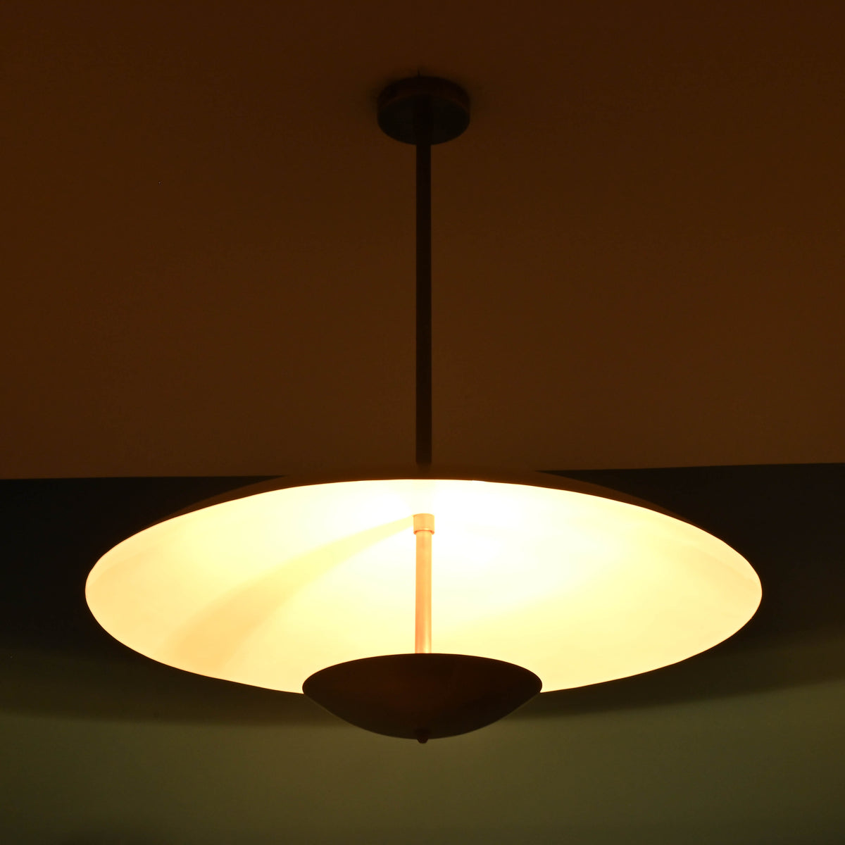 Warm lit 3 light disc style brass chandelier emphasizing minimalist form and soft ambient illumination
