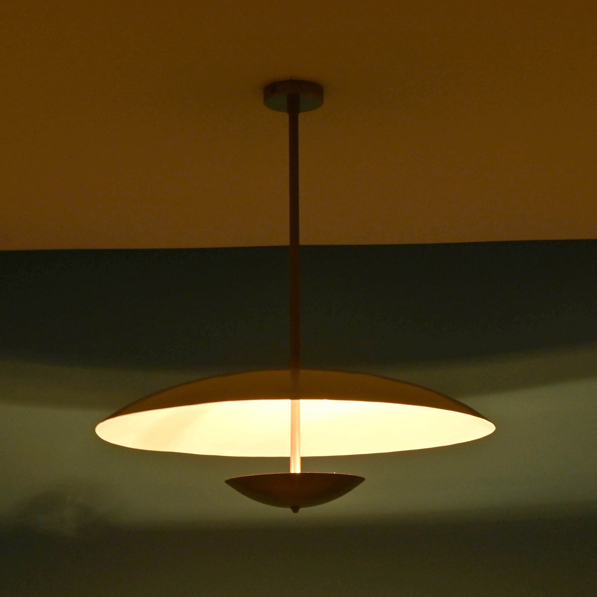 Close up night view of 3 light disc style brass chandelier showing brass bowl shade and warm glow