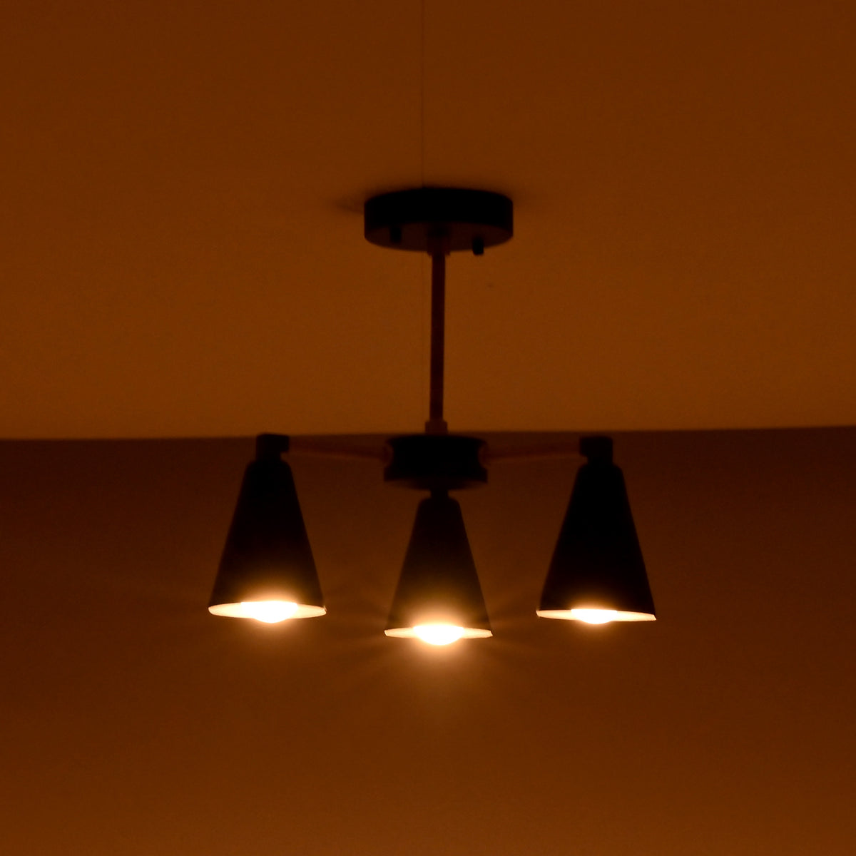 Industrial black and brass 3 light ceiling lamp glowing warmly in a dimly lit space