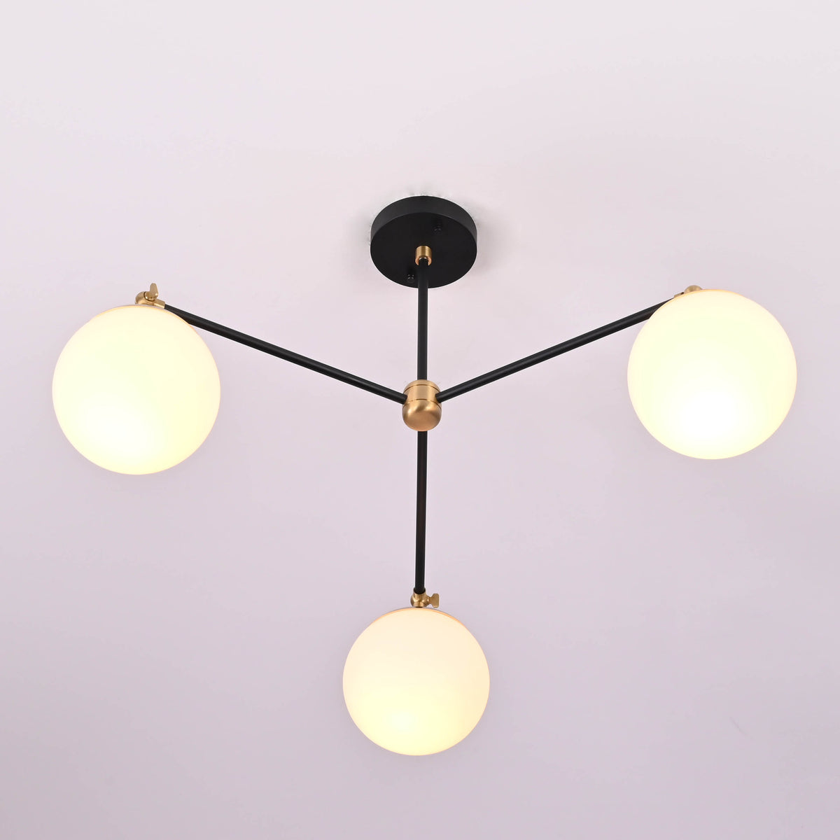 Angled perspective of a modern brass chandelier featuring three glowing opal glass globes.