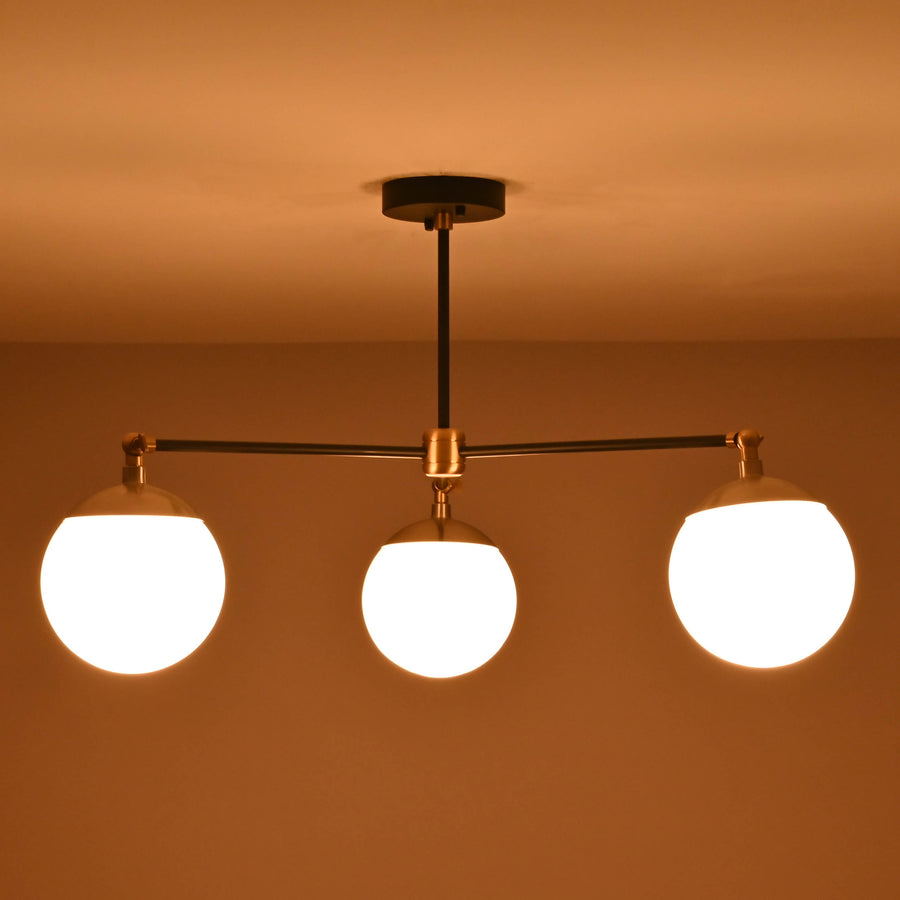 Front view of a 3 light opal glass globe brass chandelier with black arms and brushed brass accents.