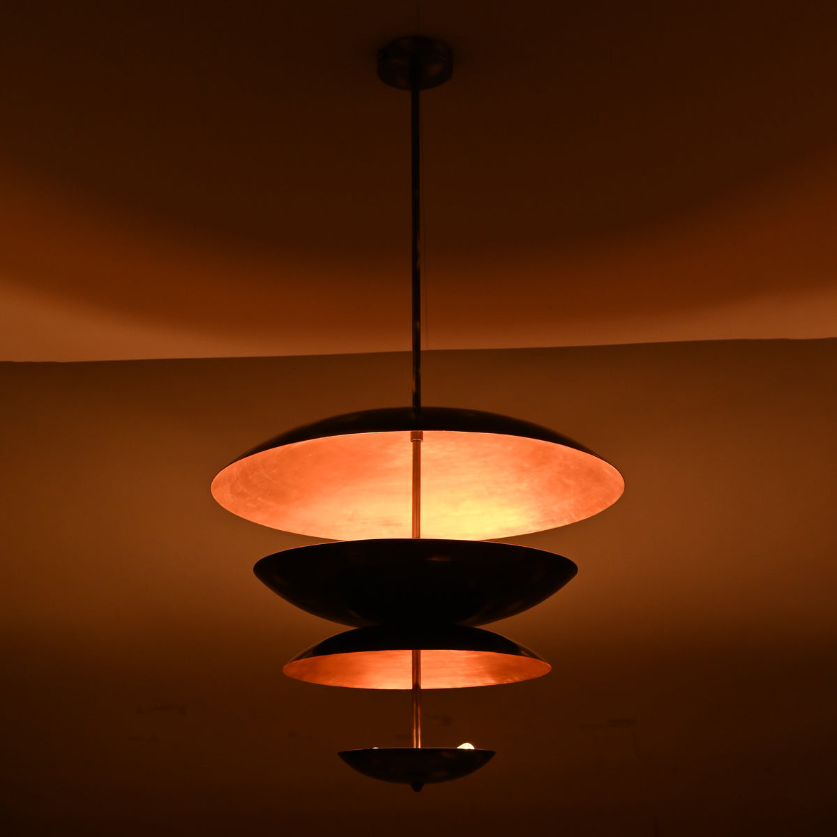 Blackened brass and copper layered pendant light glowing in low light