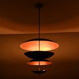 Blackened brass and copper layered pendant light glowing in low light