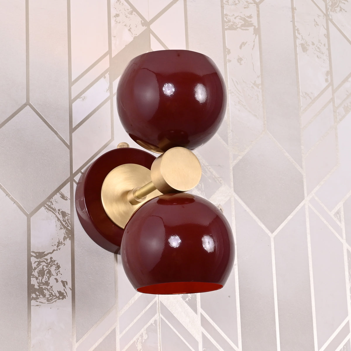 Top-down view of Brass Leaf Studio burgundy double globe wall sconce with brushed brass connector, mounted on geometric wall pattern.