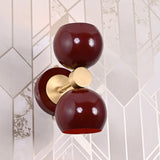 Top-down view of Brass Leaf Studio burgundy double globe wall sconce with brushed brass connector, mounted on geometric wall pattern.