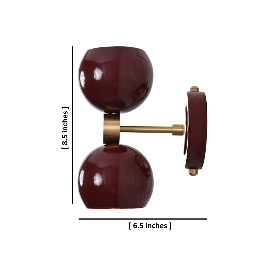 Brass Leaf Studio double globe wall sconce in deep burgundy with brushed brass accents, mounted on geometric patterned wall.