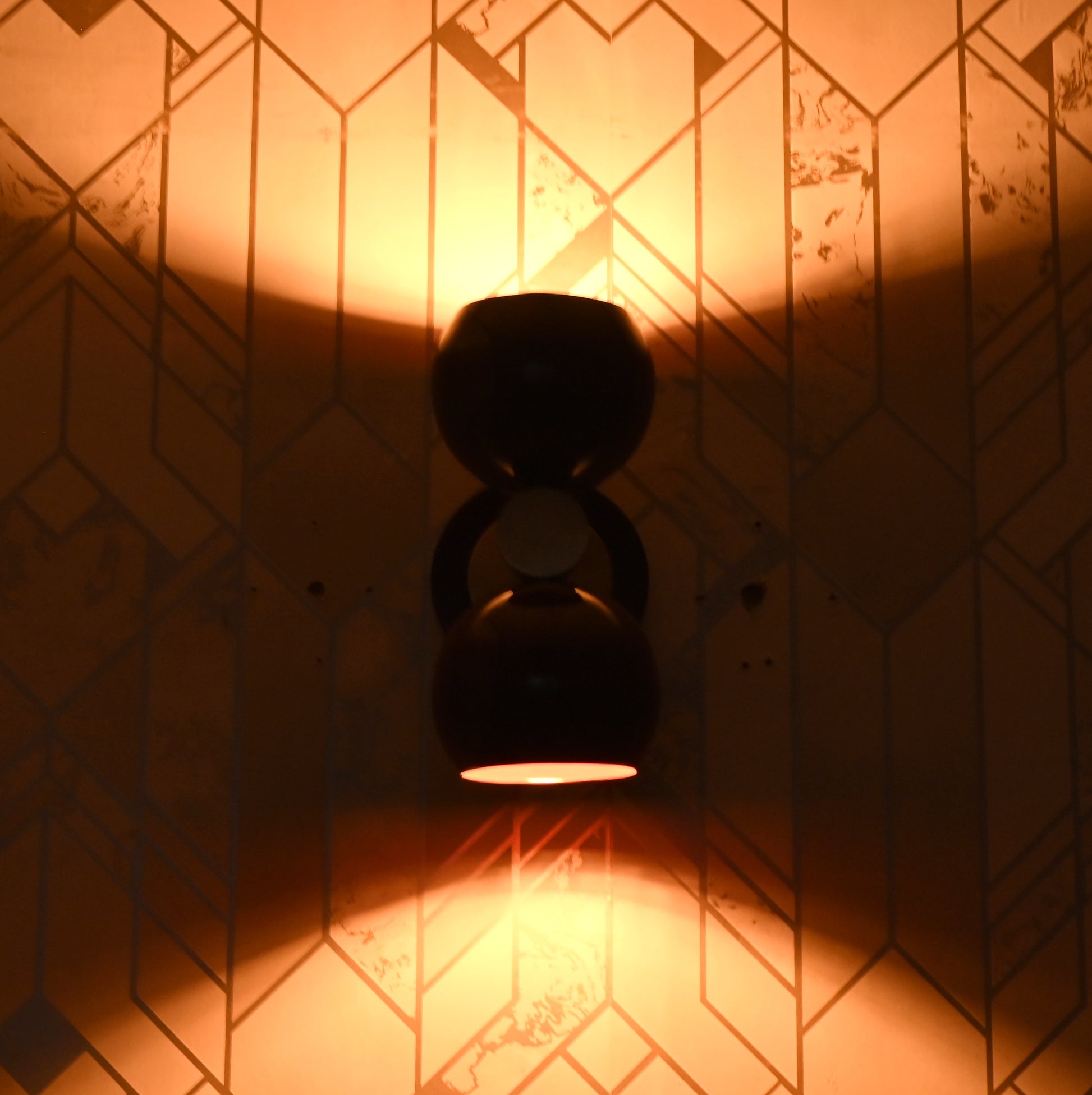 Burgundy double globe wall sconce lit up, casting warm ambient light upward and downward against patterned wall.