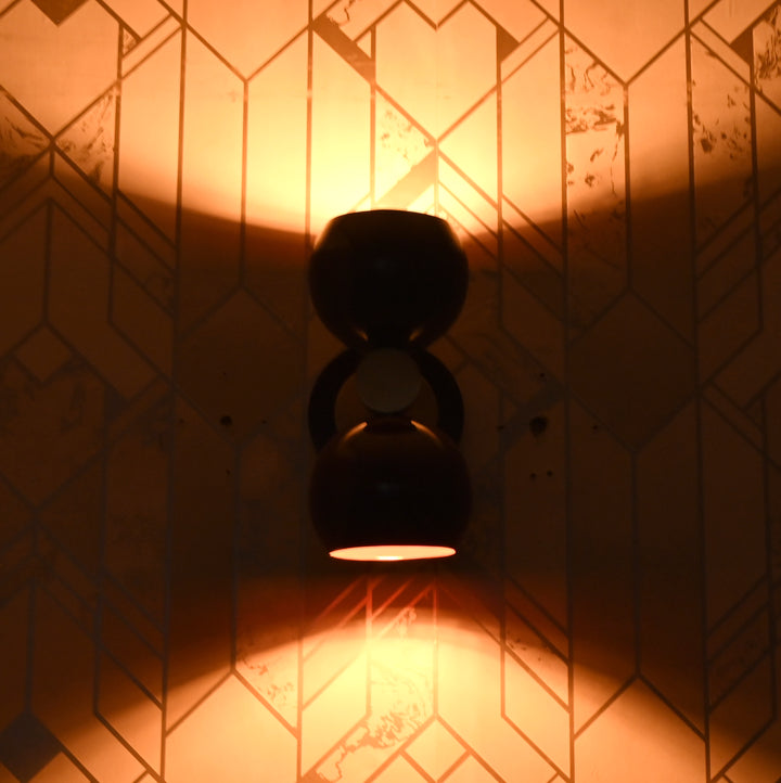 Burgundy double globe wall sconce lit up, casting warm ambient light upward and downward against patterned wall.