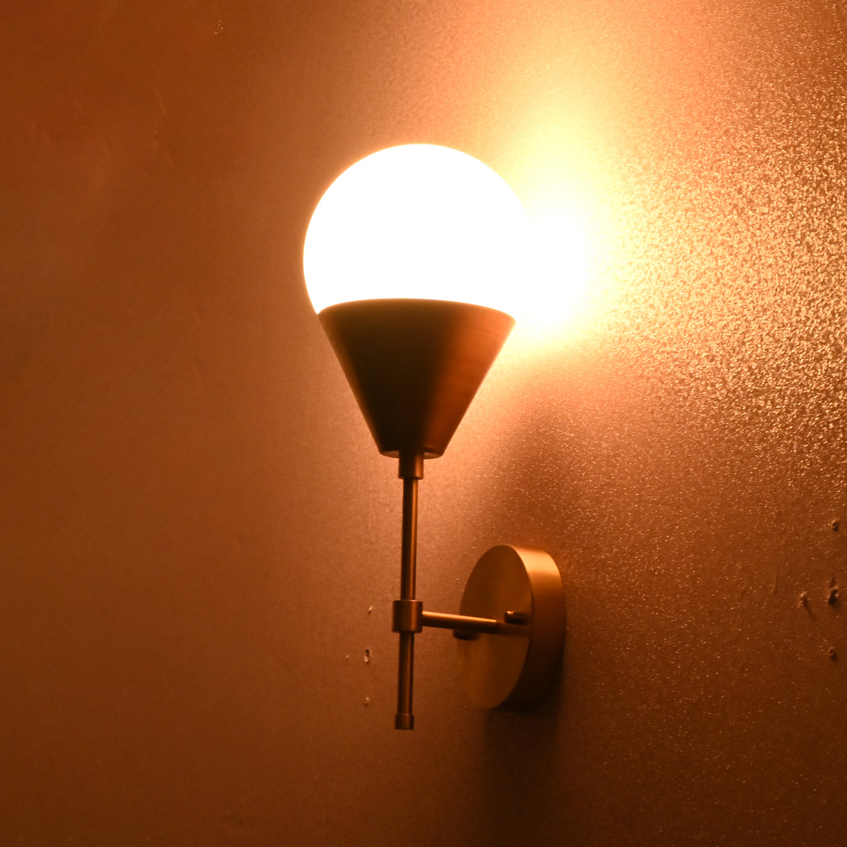 Ambient brass wall sconce with frosted globe shade, glowing warmly in a dim interior space.