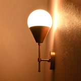 Brass wall sconce glowing warmly in dim light, featuring frosted globe shade and brass cone holder.