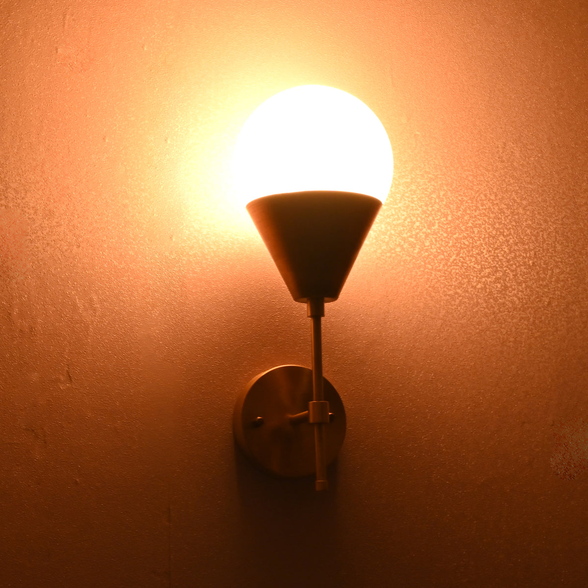 Brass wall sconce lit at night, round wall plate with frosted globe shade casting warm light.