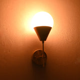 Brass wall sconce lit at night, round wall plate with frosted globe shade casting warm light.