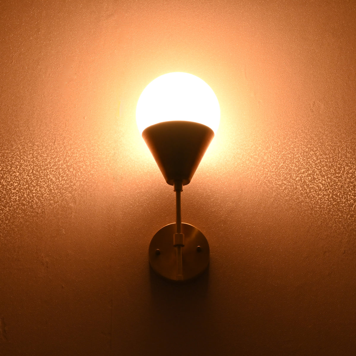 Globe-shaped brass wall sconce glowing warmly against wall, creating ambient lighting.