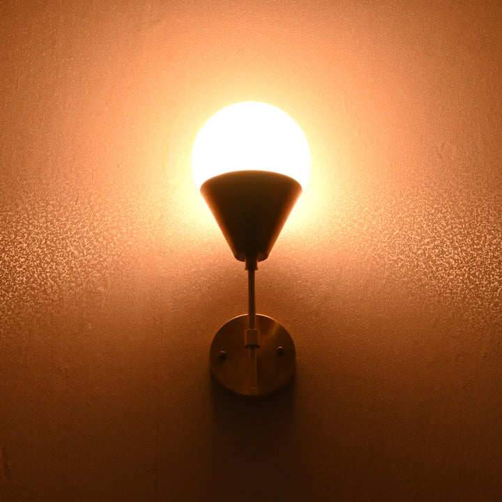Globe-shaped brass wall sconce glowing warmly against wall, creating ambient lighting.