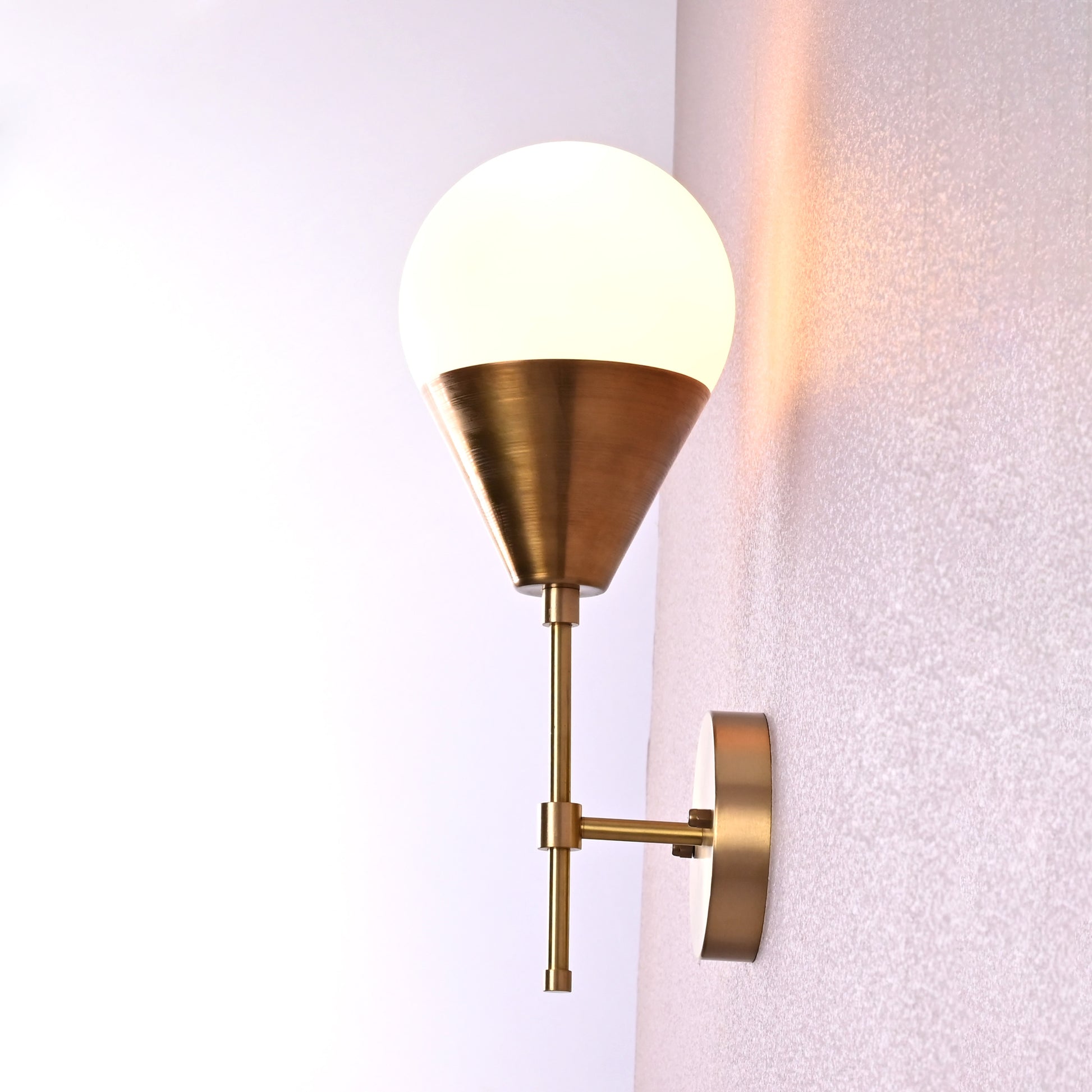 Side view of brass wall sconce with frosted globe shade and brushed brass finish.