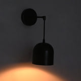 A modern black wall sconce with a dome-shaped shade and adjustable arm, mounted on a dark gray wall and casting a warm orange light downward.