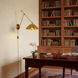 A modern wall-mounted swing-arm lamp with a fluted shade, finished in a brushed gold/brass metal.