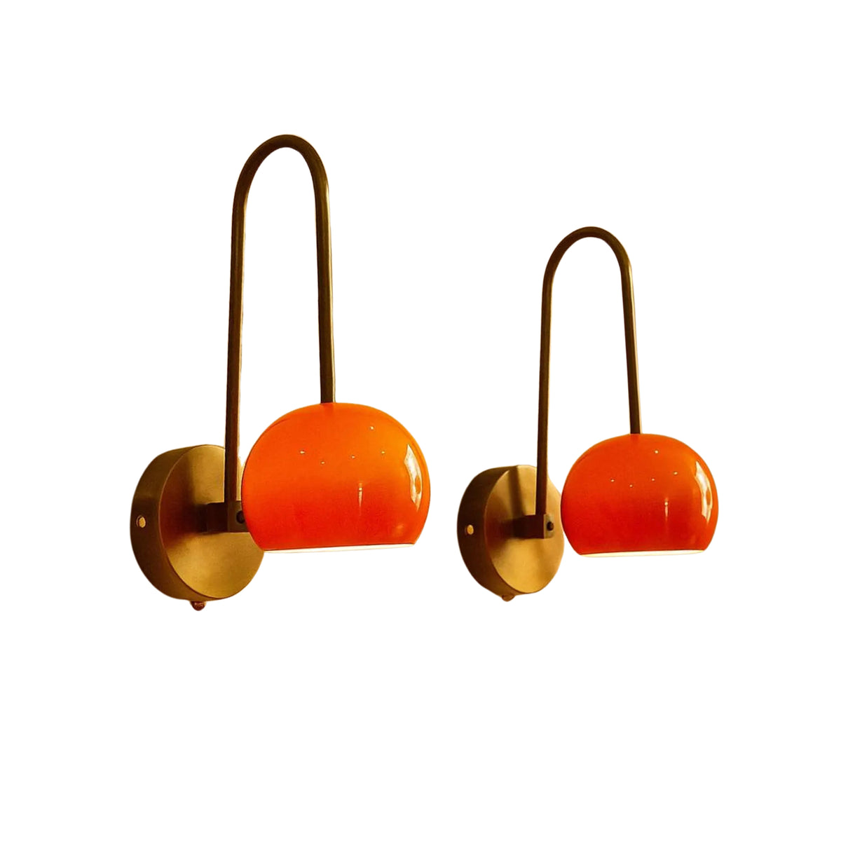 A pair of mid-century modern wall sconces with curved brass metal arms and vibrant orange glass shades, shown against a plain white background.