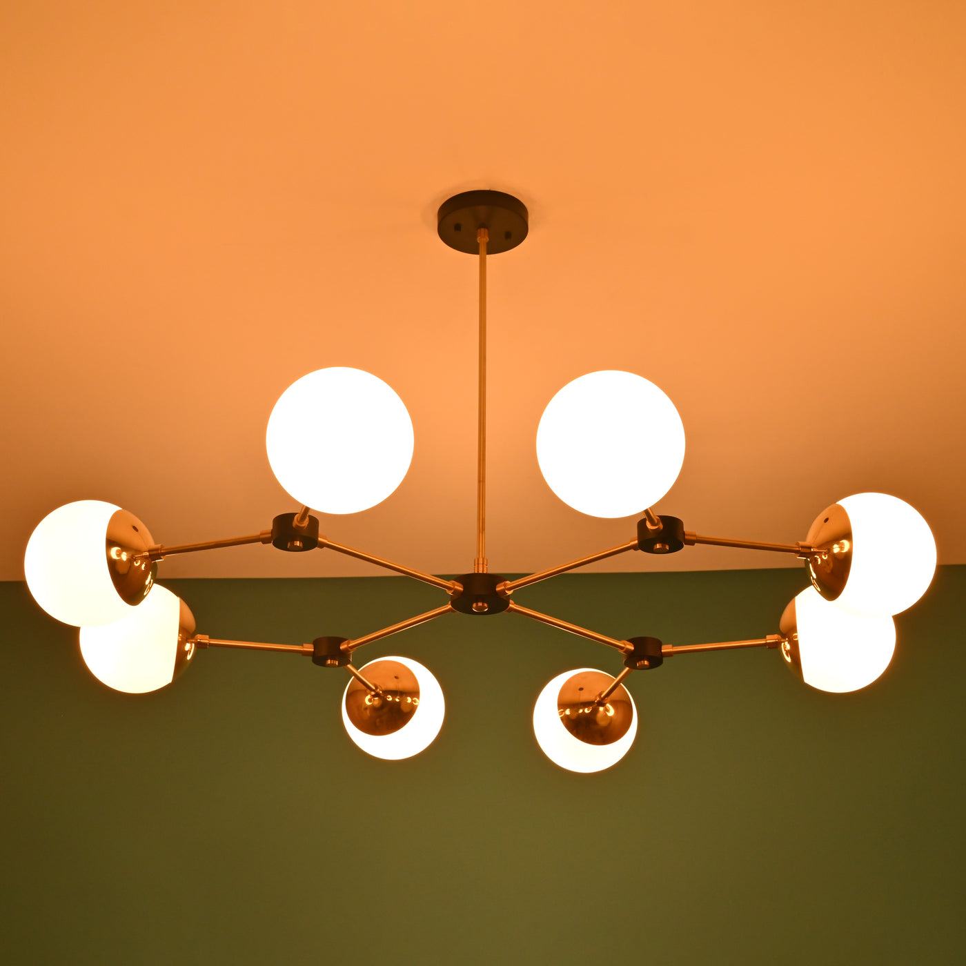  Warm-lit modern brass globe chandelier with black accents, mounted on a ceiling against a green wall background.