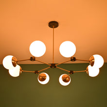  Warm-lit modern brass globe chandelier with black accents, mounted on a ceiling against a green wall background.