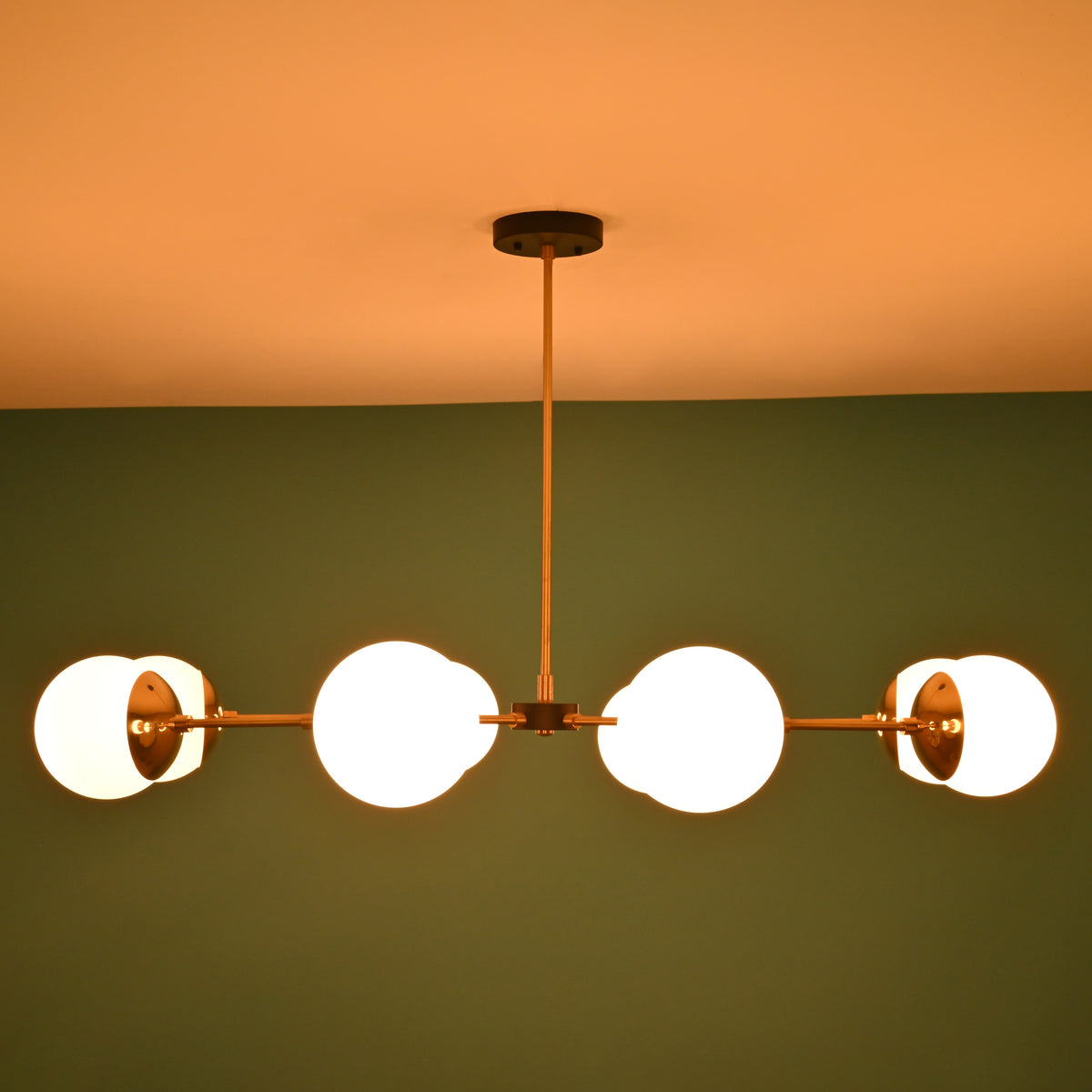 Brass and white glass globe chandelier emitting warm light, set against a green wall background in low lighting.