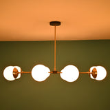 Brass and white glass globe chandelier emitting warm light, set against a green wall background in low lighting.