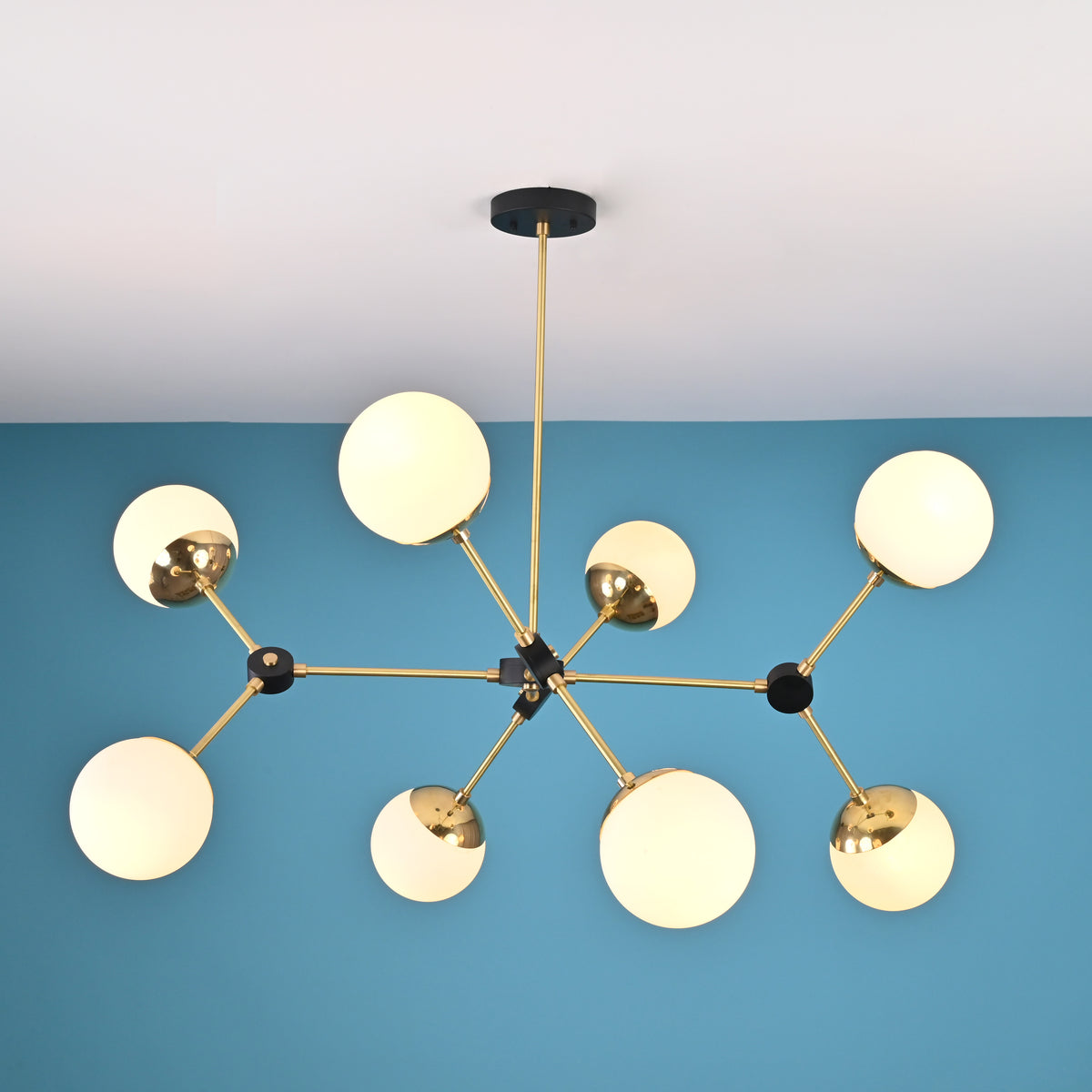 Overhead view of a brass and black modern chandelier with eight frosted glass globe shades in a geometric arrangement