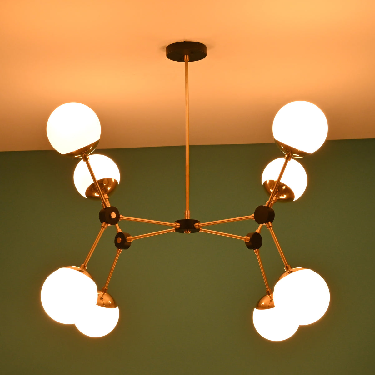 Black and brass eight-light chandelier with glowing white glass globes, photographed in a dim-lit setting.