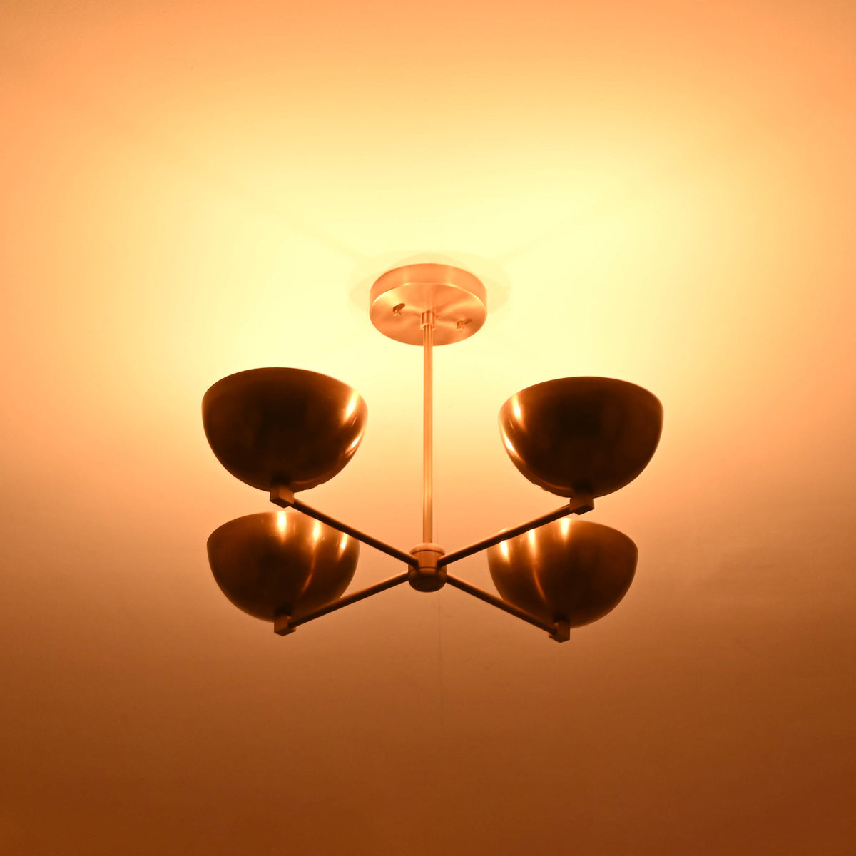 Angled dark-room view of a handcrafted 4 bowl brass chandelier showing soft ambient illumination and refined brass detailing.