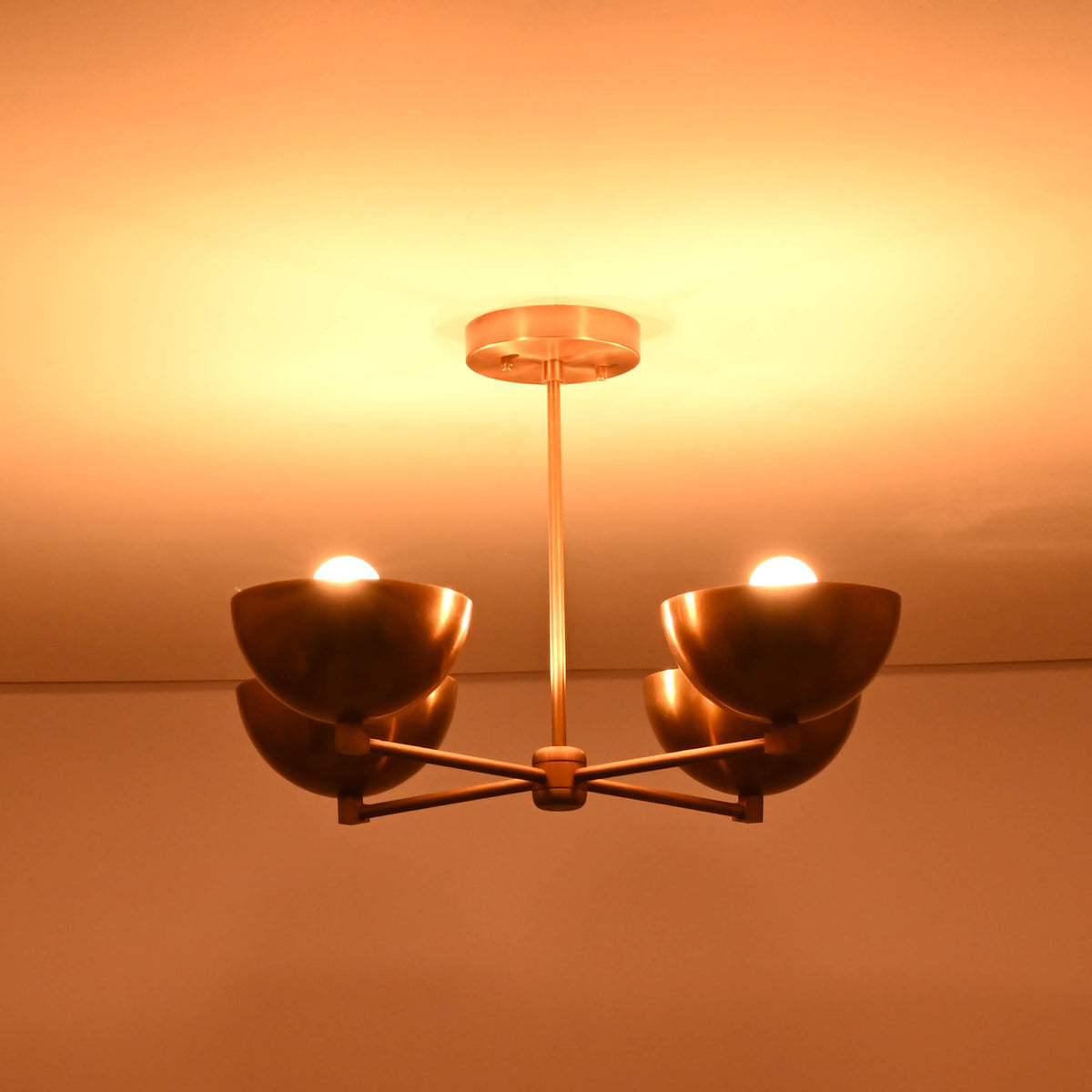Bottom perspective of a 4 bowl brass chandelier glowing in a warm light, highlighting its minimalist geometry and premium brass finish.