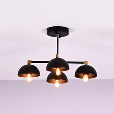 Side view of modern 4 light flush mount chandelier with black dome shades and brass accents
