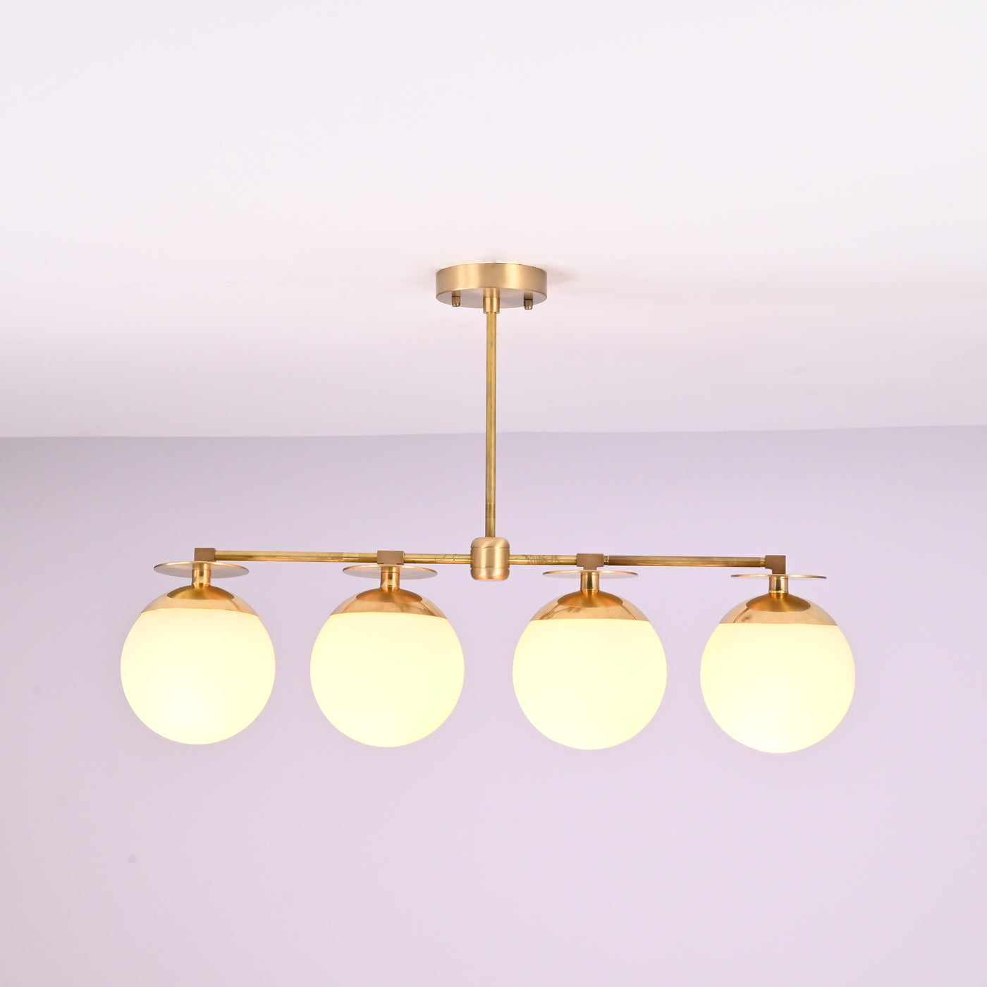 Front view of 4 linear brass chandelier with opal glass globe shades, showcasing minimalist industrial design and warm ambient lighting.