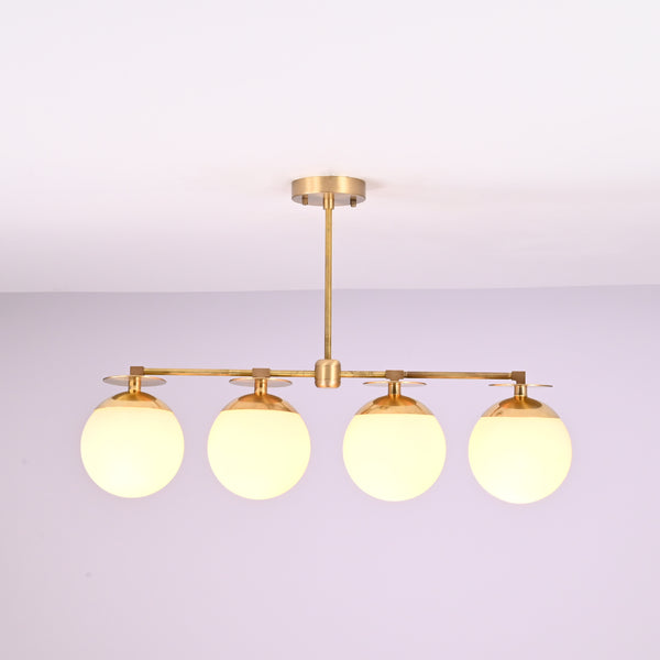 Front view of 4 linear brass chandelier with opal glass globe shades, showcasing minimalist industrial design and warm ambient lighting.