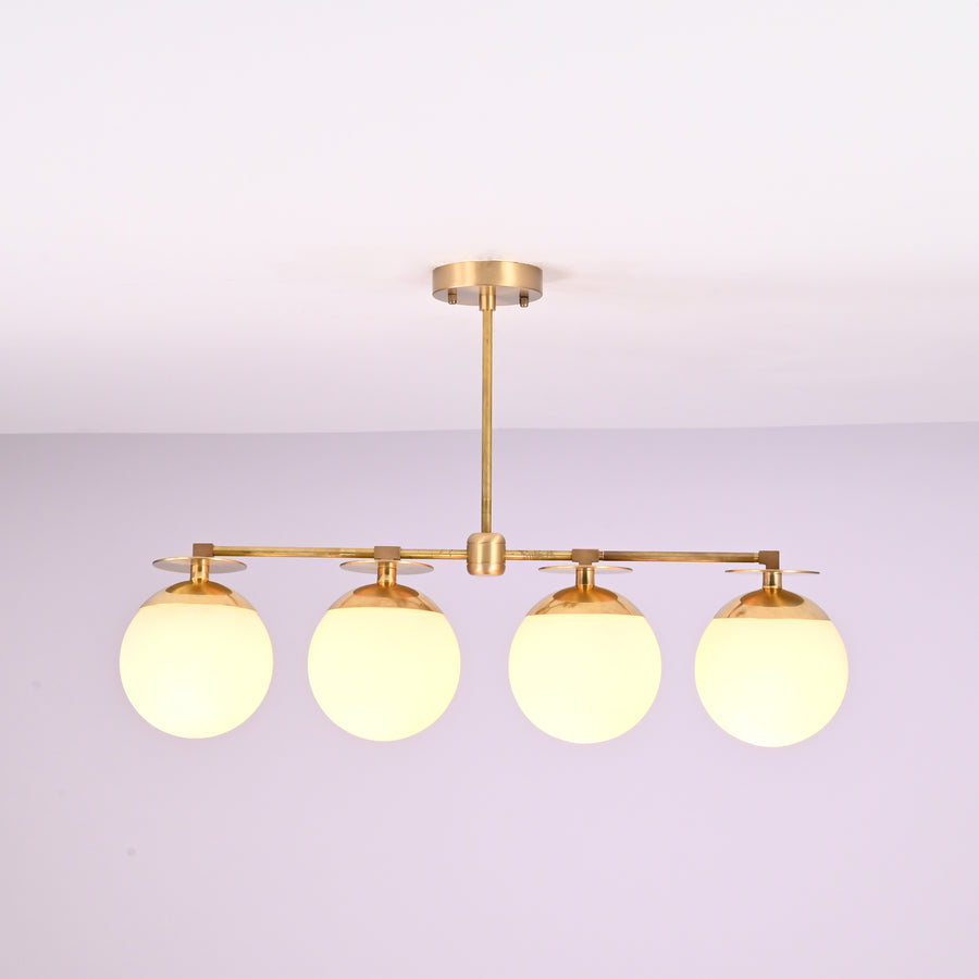 Front view of 4 linear brass chandelier with opal glass globe shades, showcasing minimalist industrial design and warm ambient lighting.