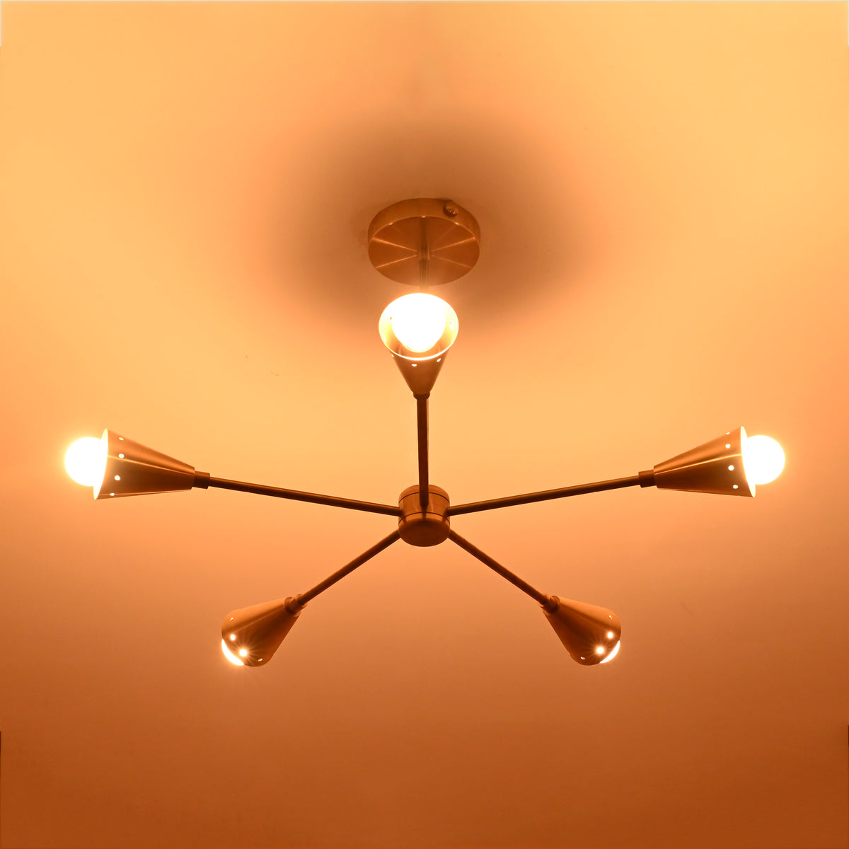 Lit view of handcrafted brass ceiling chandelier with five conical light arms, creating a golden modern glow in luxury interior spaces.