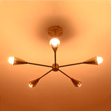 Lit view of handcrafted brass ceiling chandelier with five conical light arms, creating a golden modern glow in luxury interior spaces.
