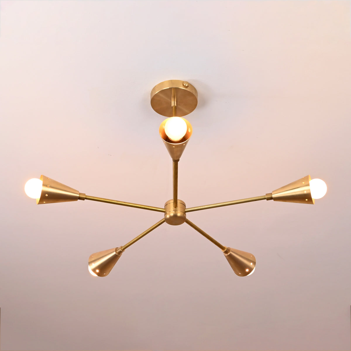 Overhead top view of 5-light brass ceiling fixture displaying perfect symmetry and modern geometric form in brushed brass with soft ambient glow.
