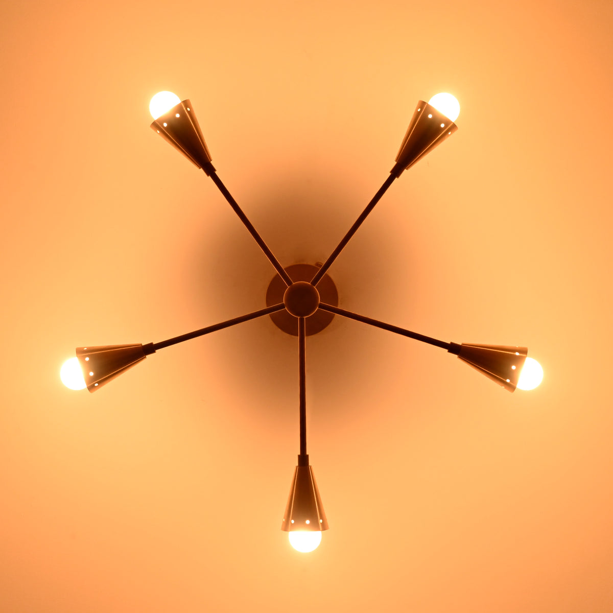 Illuminated 5-light brass cone chandelier casting warm ambient light with mid-century style elegance, ideal for refined home and commercial interiors.